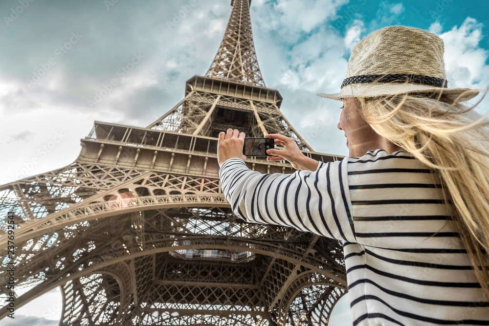 Woman tourist selfie near the Eiffel Tower in Paris under sunlight - obrazy, fototapety, plakaty 