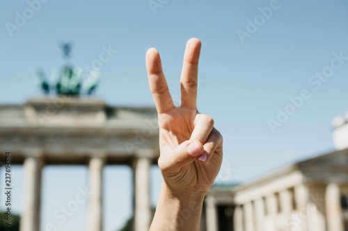 The girl shows peace sign on the background of the Brandenburg Gate in Berlin in Germany. © franz12