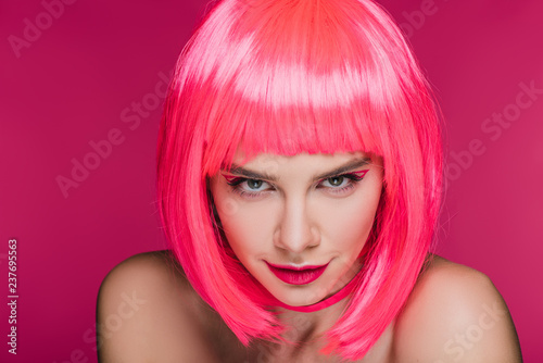 beautiful sly girl in neon pink wig looking at camera, isolated on pink