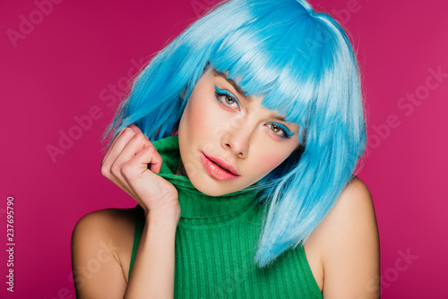 attractive stylish girl posing in blue wig and green turtleneck, isolated on pink