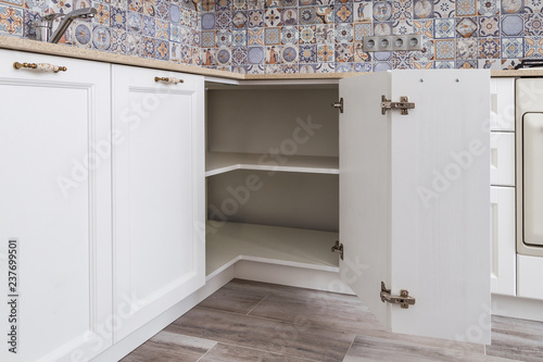 Solution for a kitchen corner in a cupboard. The angular opening with corner hinges. Classical kitchen interior, white wooden fronts and thin quartz countertop.