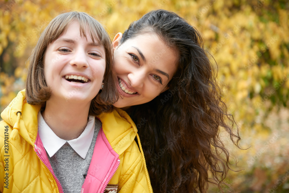 Fototapeta premium Portrait of pretty woman and teen girl. They are posing in autumn park. Beautiful landscape at fall season.