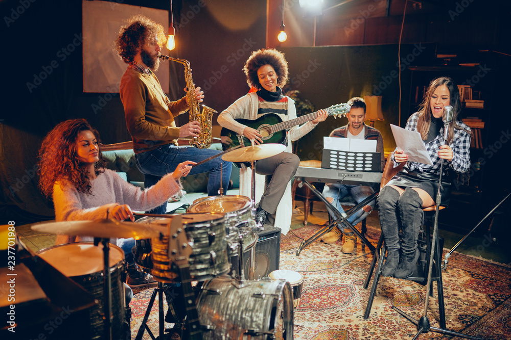 Fototapeta premium Band practice in home studio. Woman singing while rest of the band playing instruments.