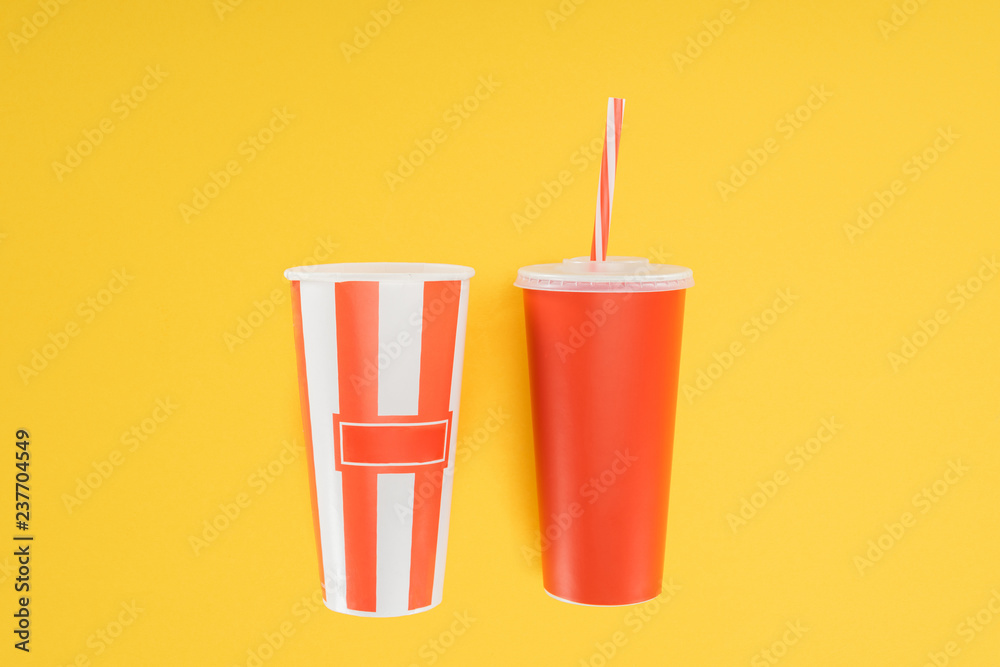 striped popcorn bucket and red disposable cup with straw isolated on yellow striped popcorn bucket and red disposable cup with straw isolated on yellow
