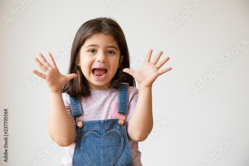 Excited preschooler child screaming and showing palms. Cute joyful Hispanic kid with funny grimace. Isolated on white with copy space. Having fun concept photo
