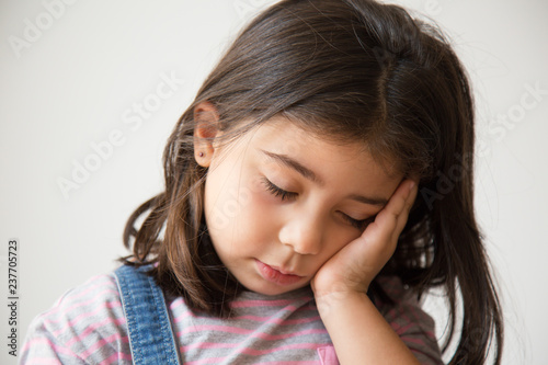 Tired Latin kid with closed eyes sleeping on hand. Exhausted Hispanic little girl. Isolated on white. Sleep concept