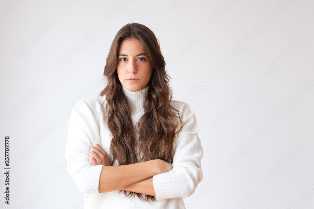 Serious Hispanic girl with crossed arms and long hair looking at camera. Portrait of beautiful confident young woman. Isolated on white. Confidence concept Serious Hispanic girl with crossed arms and long hair looking at camera. Portrait of beautiful confident young woman. Isolated on white. Confidence concept