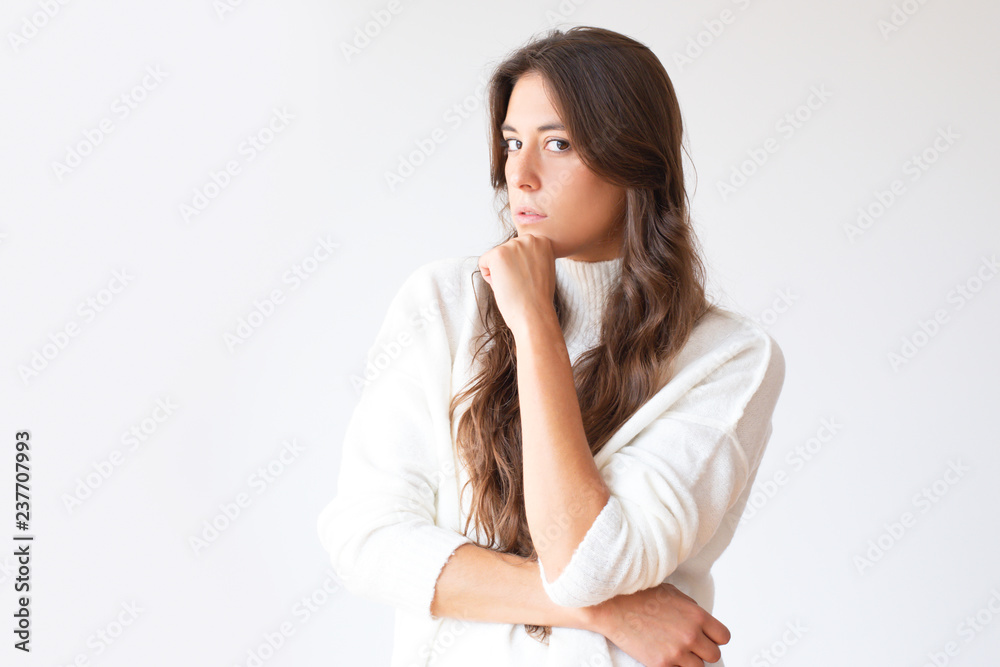 Thoughtful Hispanic woman with long hair holding chin and looking at camera. Beautiful pensive Latin girl in trendy sweater. Isolated on white. Thinking concept Thoughtful Hispanic woman with long hair holding chin and looking at camera. Beautiful pensive Latin girl in trendy sweater. Isolated on white. Thinking concept