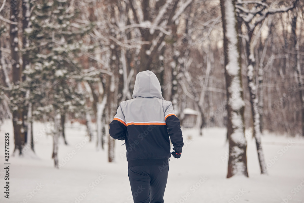 Man jogging in a cold winter snowy day outdoors.