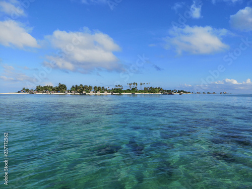 Stunning view of the ocean with coral reef, blue sky and island background.