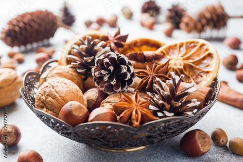 Winter food ingredients nuts cones oranges cinnamon star anise in a bowl. Rustic style.