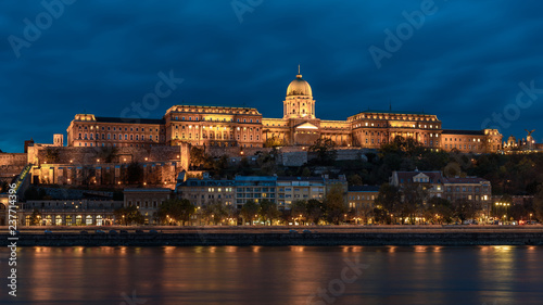 Buda Castle, overlooking the river Danube, in Budapest. The castle is lit up at night time, with the lights reflecting on the river