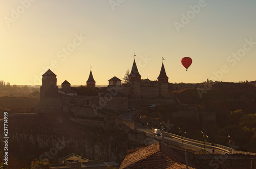 Hot air balloon flies near Kamianets-Podilskyi castle. It is famous touristic place and romantic travel destination. Beautiful autumn sunset landscape. Kamenetz Podolsky, Khmelnitsky region, Ukraine © evgenij84