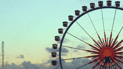 Giant spinning ferris wheel at sunset, silhouetted against an evening sky with clouds and colorful blinking lights at an amusement park at christmas.