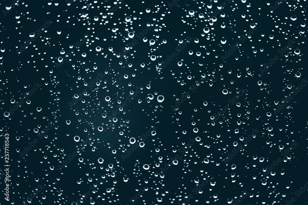 Obraz premium Dirty window glass with drops of rain. Atmospheric blue background with raindrops. Droplets and stains close up. Detailed transparent texture in macro with copy space. Rainy weather.