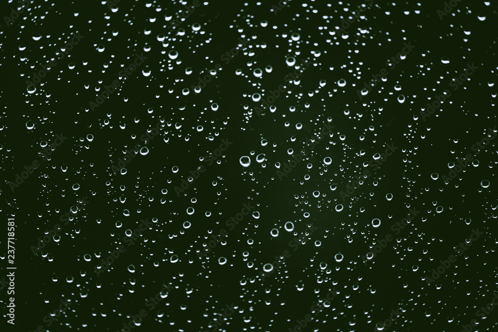 Obraz premium Dirty window glass with drops of rain. Atmospheric green background with raindrops. Droplets and stains close up. Detailed transparent texture in macro with copy space. Rainy weather.