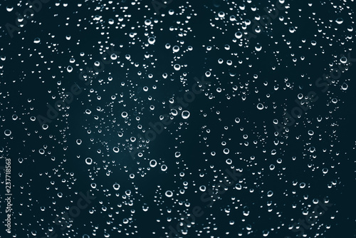 Dirty window glass with drops of rain. Atmospheric blue background with raindrops. Droplets and stains close up. Detailed transparent texture in macro with copy space. Rainy weather.