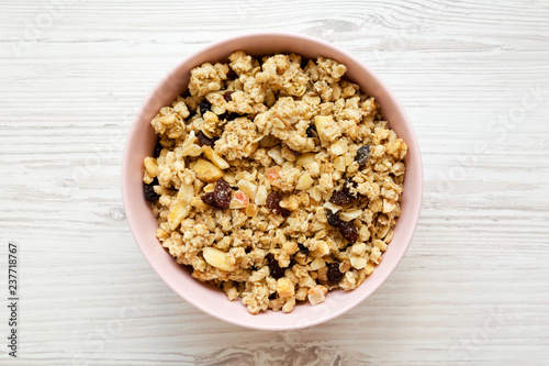 Pink bowl of fruit granola over white wooden surface, overhead view. Closeup.