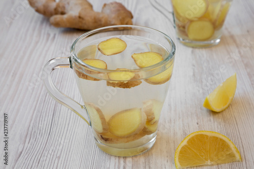 A mug of homemade ginger tea with lemon on white wooden surface, side view.