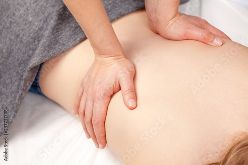 Tween girl receiving osteopathic treatment or medical massage of lumbar region on her back