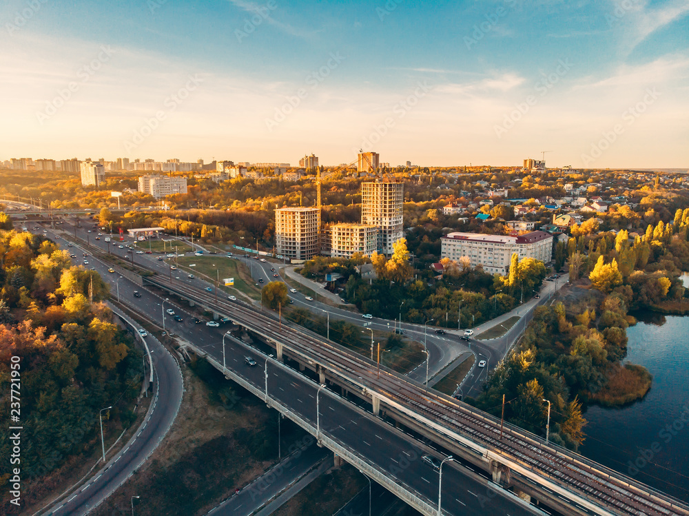 Asphalt road and bridge in city, transport junction with car traffic at sunset cityscape background, aerial view from drone