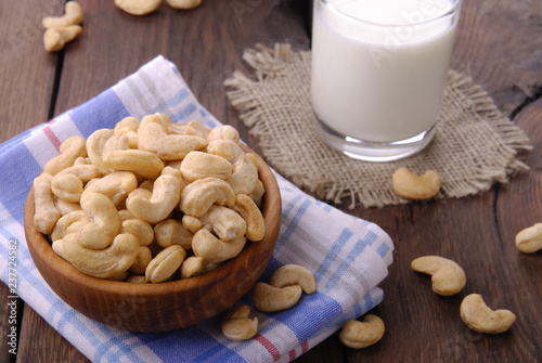 Raw cashews in a wooden bowl and a glass of milk on a wooden background.