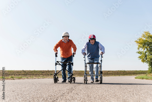 Two old friends wearing safety helmets, competing in a wheeled walker race photo