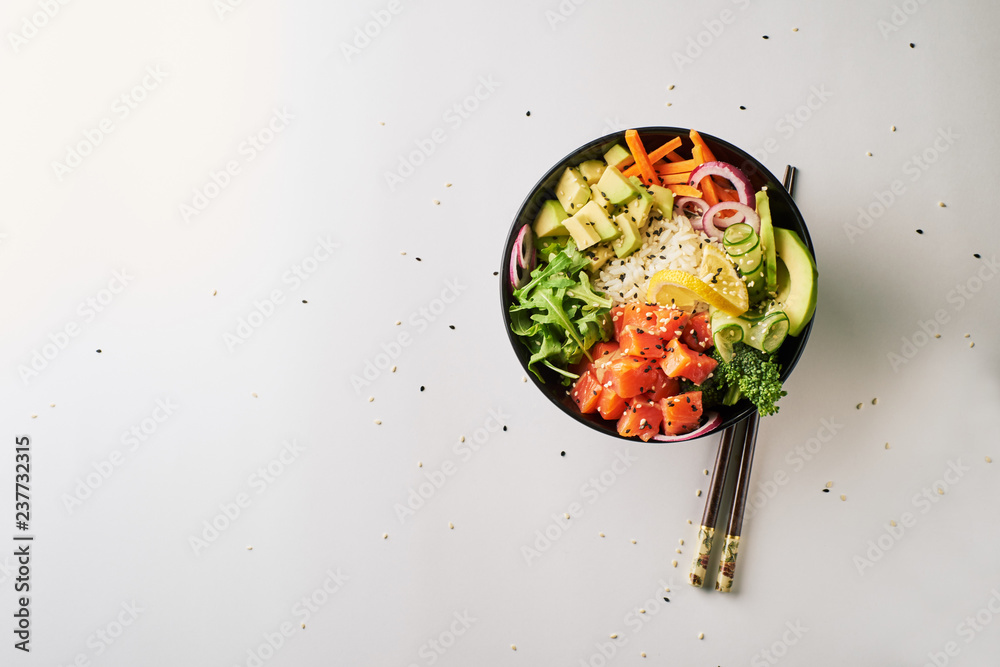 poke bowl with salmon, avocado, cucumber, arugula, broccoli, rice, carrot and sweet onions with chopsticks isolated over white background. top view