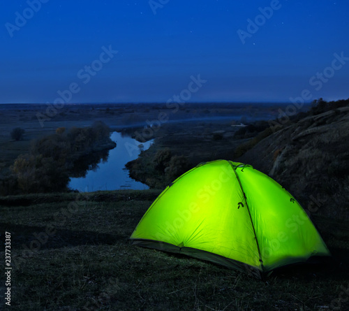 Lighted from the inside green tents on hill above river © alexlukin