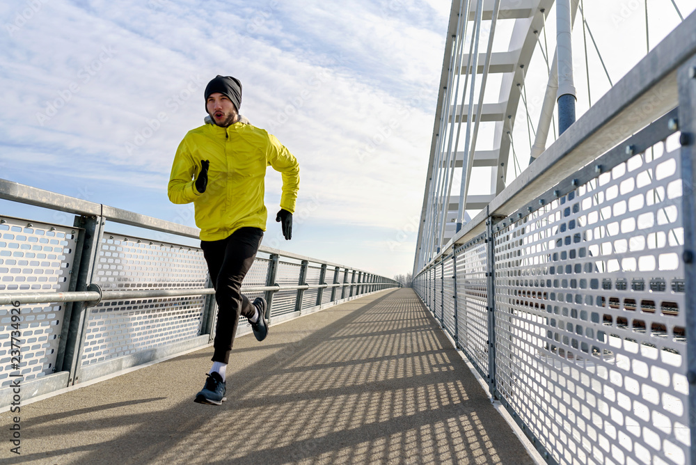Attractive fit man running fast along big modern bridge. Exercising, Jogging, Sport, Winter. Male athlete running. Attractive fit man running fast along big modern bridge. Exercising, Jogging, Sport, Winter. Male athlete running.