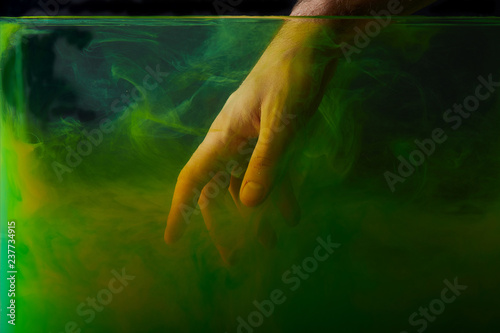cropped view of man putting hand into water with green paint