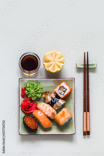 sushi rolls Asian food on a square green plate with wasabi and ginger, soy sauce on white background with lemon