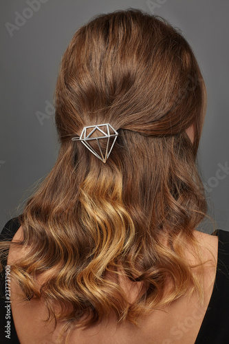 Close up isolated portrait of a young lady with brown ombre hair colour. The back view of the girl with half-up hairstyle, adorned with silver diamond shaped barrette. Posing on the grey background.