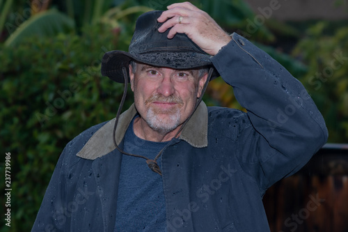 Portrait of senior man standing the rain wearing raincoat and cowboy hat outdoors