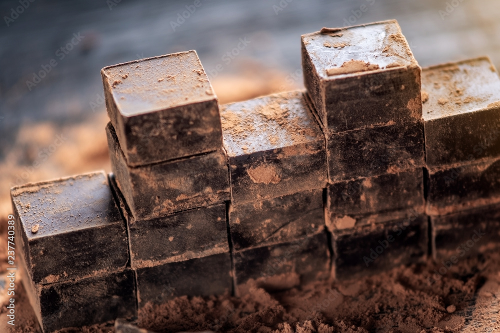 Pieces of dark bitter chocolate with cocoa powder on dark wooden background. Concept of confectionery ingredients Pieces of dark bitter chocolate with cocoa powder on dark wooden background. Concept of confectionery ingredients