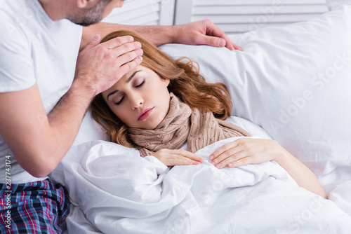 husband touching forehead of sick wife with fever in bed