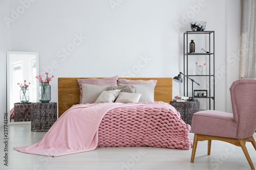 Pink cozy woolen blanket and duvet on comfortable king size bed in fashionable bedroom interior