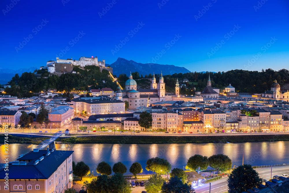 View of cityscape of Salzburg Cathedral, Fortress Hohensalzburg, and old castle in center of old town with river and road along the river at sunset time in Salzburg, Austria, Europe