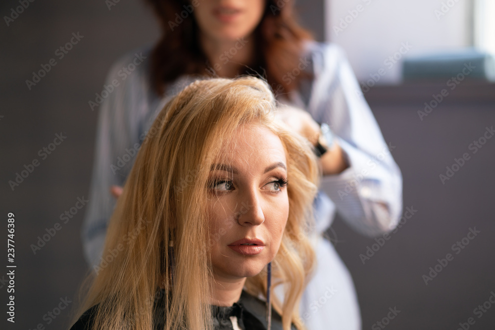 Fototapeta premium beautiful adult blonde client sits in a chair while a hairdresser master in the salon does her hair with a corrugation and a Perm