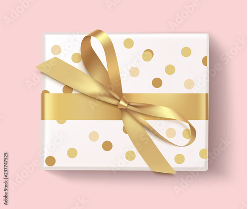 Decorative white gift box with golden bow and ribbon isolated on pink. Christmas or New Year decoration. Top view.