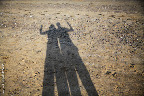 Shadow of a couple on a beach holding their arms in the air 