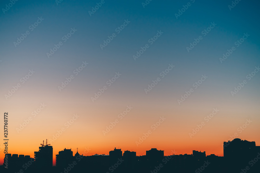 Cityscape with wonderful varicolored vivid dawn. Amazing blue sky with orange sunny light above dark silhouettes of city buildings. Atmospheric background of warm sunrise. Copy space.