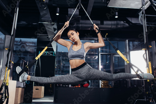 attractive asian sportswoman doing split with resistance bands at gym