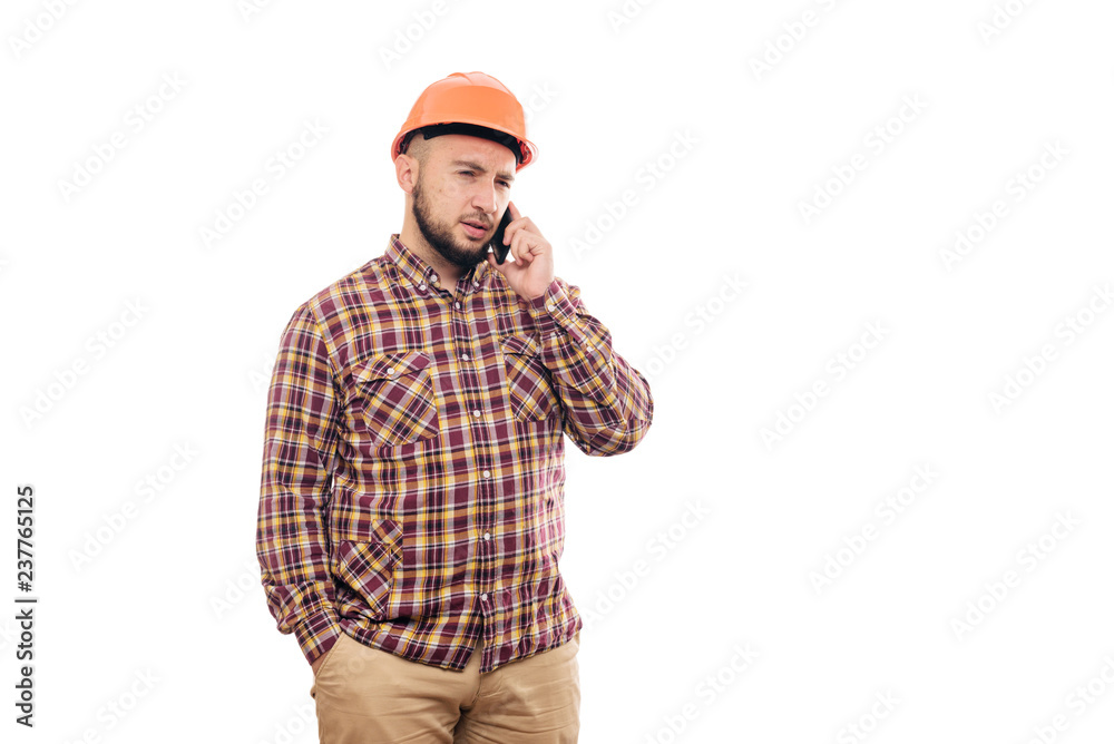 An angry and nervous worker in an orange helmet is talking loudly on the phone, shouting into the phone. Isolated white background