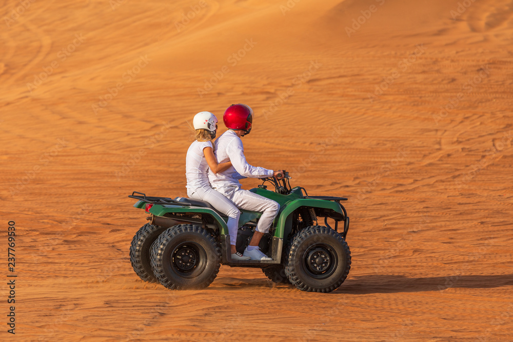 Quad Biking Dubai Adventure Tour – Young copule of tourists having fun on Quad Bike Riding in dunes of Dubai Quad Biking Dubai Adventure Tour – Young copule of tourists having fun on Quad Bike Riding in dunes of Dubai