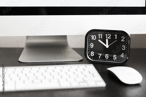 Computer with white keyboard and black clock on wooden table. Template photo