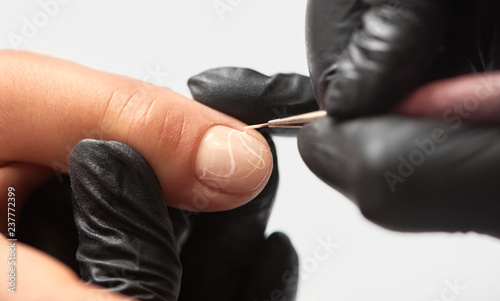 Fashionable manicure in beauty salon. Close-up of professional manicurist hands in black rubber gloves painting elegant abstract patterns on client woman nails using applicator on white background.
