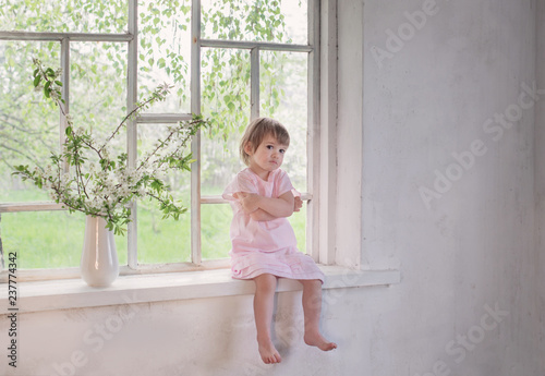beautiful little girl on old windowsill with spring flowers