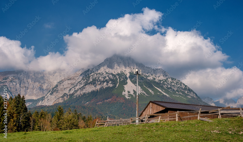 Alpine landscape on a sunny day. Colorful autumn scene. Mountain and a huge cloud above it. In the foreground is a relay tower and an alpine shed. Amazing natural background. South Tyrol Austria