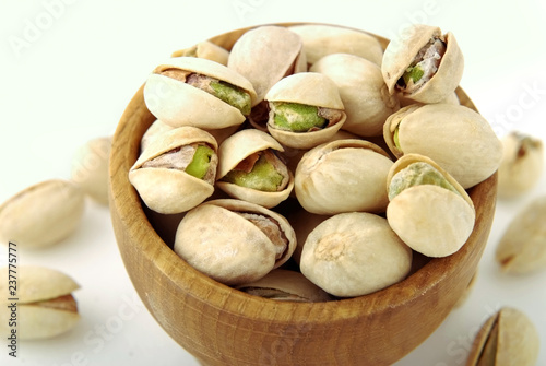 Salted pistachios in a wooden bowl on a white isolate.